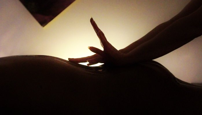 A picture in silhouette showing Francesca's hands sliding along the back of lady lying on her massage table